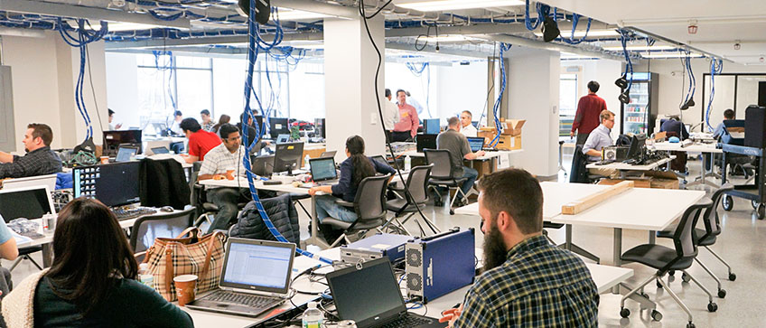 Plugfest attendees gathered around computers and other equipment